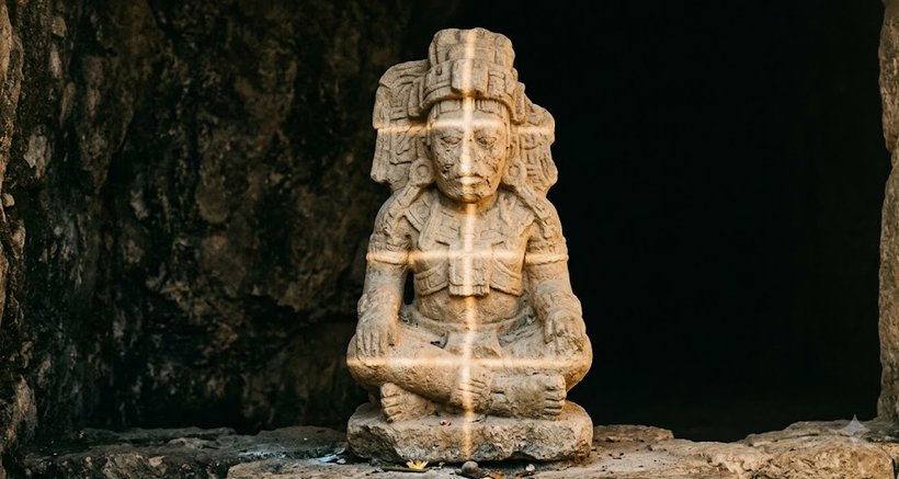 A seated Maya stone figure lit by a shaft of light